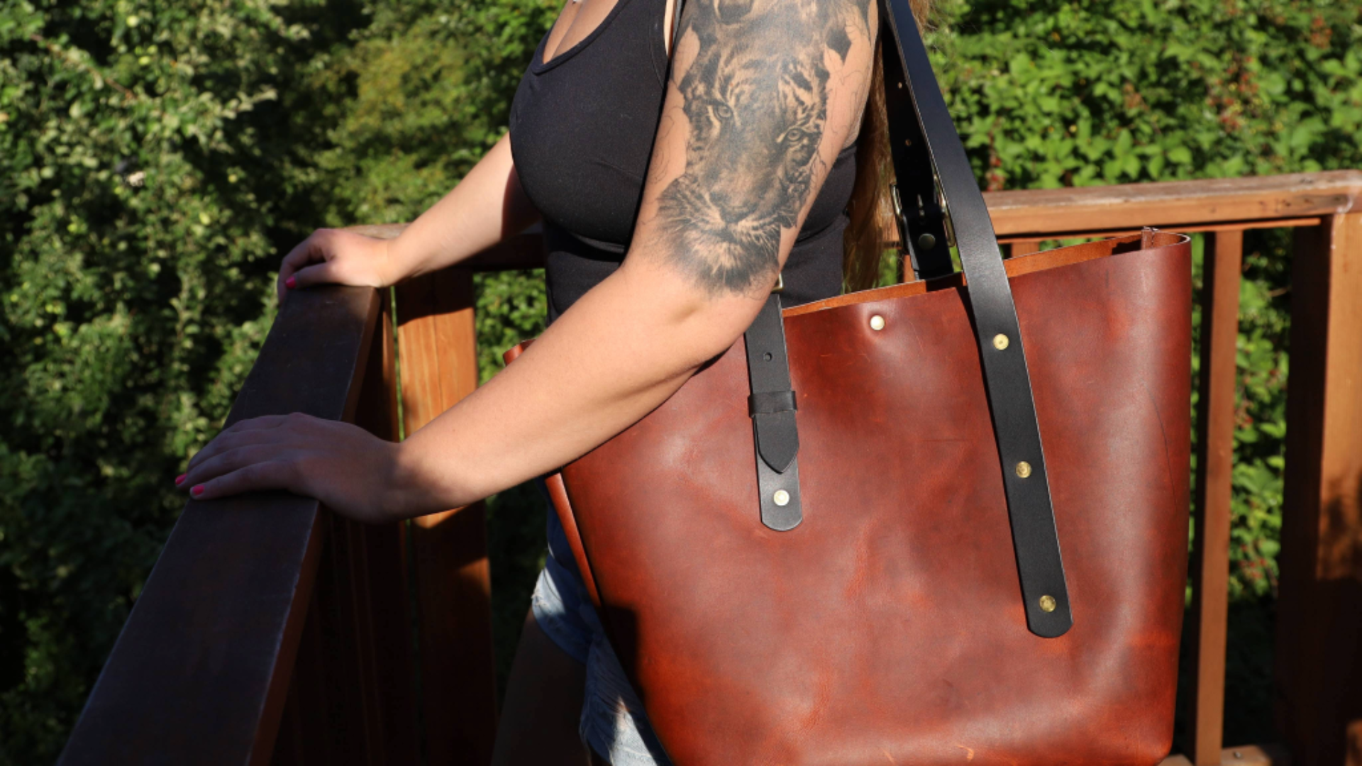 woman with tattoo standing next to wood railing with dry fly leather goods tote bag on her shoulder